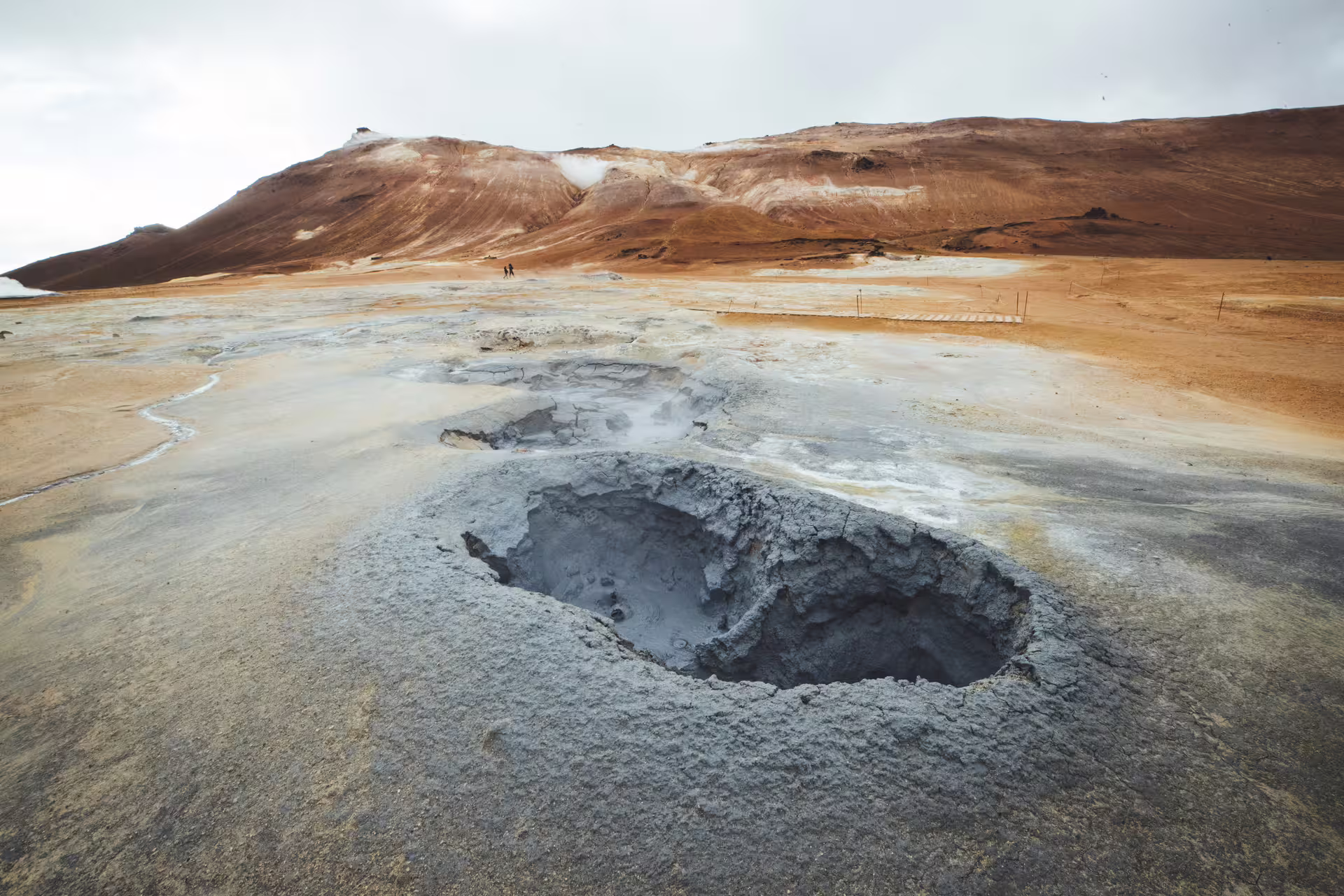 Bubbling mud pool at geothermal area with rust-colored hills in North Iceland Diamond Circle