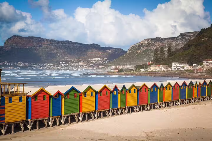 Colorful beach huts at Muizenberg Beach against scenic mountain backdrop, perfect for Cape Town tour enthusiasts.