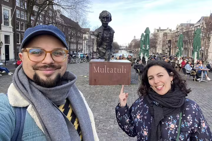 Couple posing at Multatuli statue along Amsterdam canal on self-guided walking tour