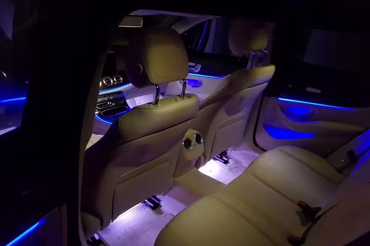 Luxury car interior with blue ambient lighting and beige leather seats for private transfer