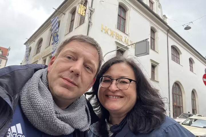 Couple smiling in front of Hofbräuhaus brewery in Munich on a cloudy day