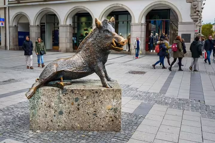 Bronze wild boar sculpture on stone pedestal in Munich pedestrian square with shoppers in background