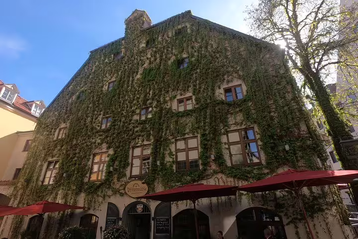 Historic ivy-covered building in Munich old town with outdoor restaurant seating below