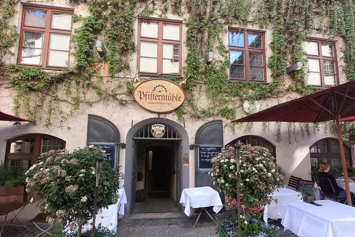 Pfistermühle historic restaurant exterior with ivy-covered walls and outdoor dining tables in Munich