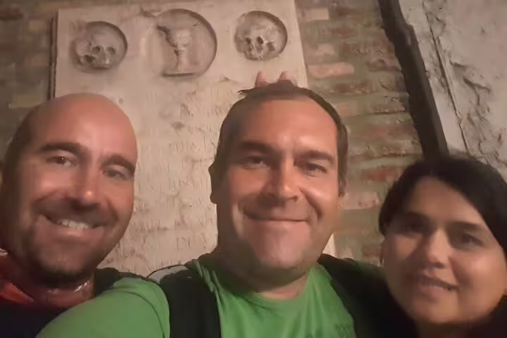 Three smiling tourists posing in front of ancient stone skull carvings during Munich haunted walking tour