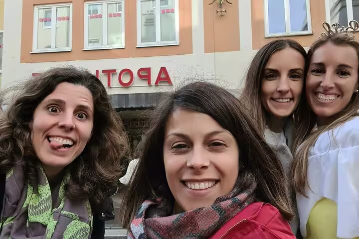 Four smiling women taking a selfie on a Munich street in front of an Apotheke pharmacy building
