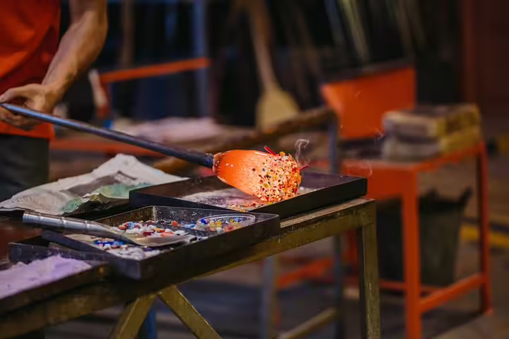 Glassblower crafting vibrant piece in Murano on Grand Canal tour, showcasing intricate artistry and tradition.