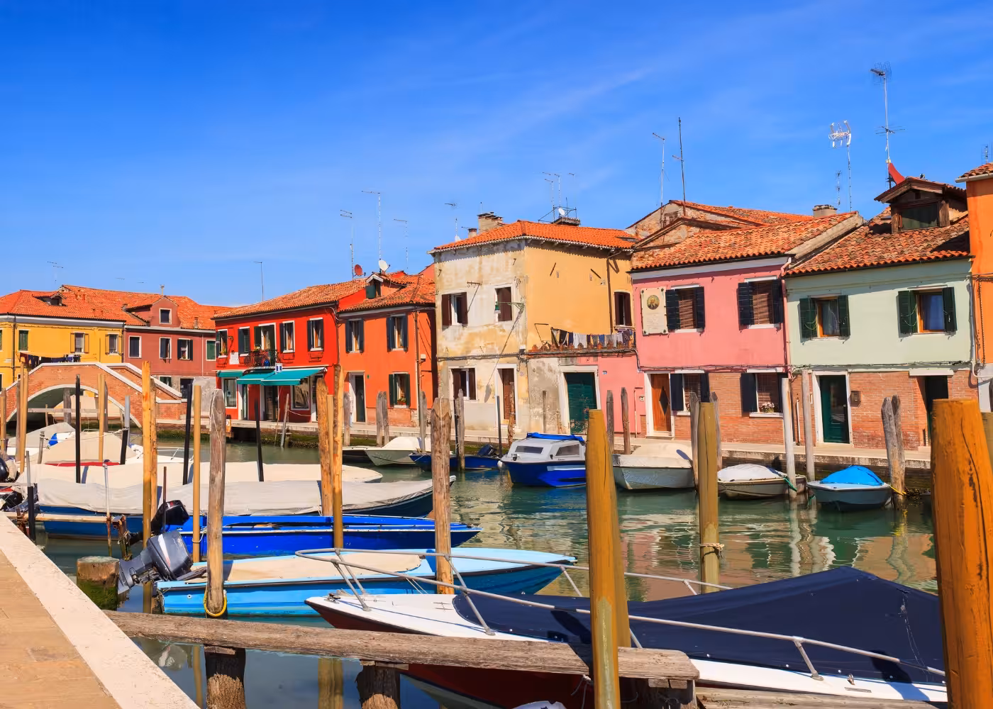 Scenic view of vibrant houses and boats along the canal on Murano Island, highlighting its charming atmosphere.