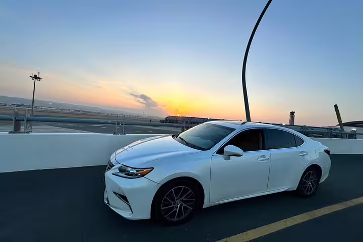 White car at Muscat Airport during sunset, offering convenient taxi transfer services to local hotels for travelers.