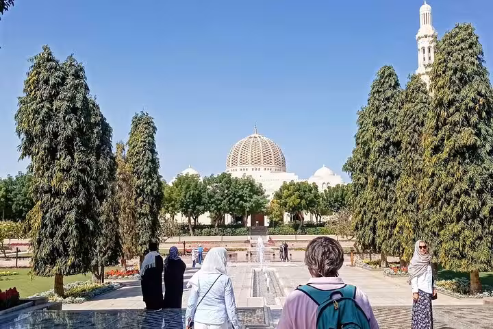 Visitors walk through manicured gardens toward Sultan Qaboos Grand Mosque on a sunny half-day Muscat city tour in Oman