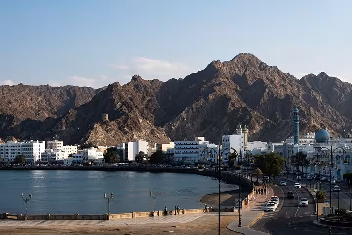 Scenic Muscat corniche waterfront with mosque white buildings and rugged mountains on city tour