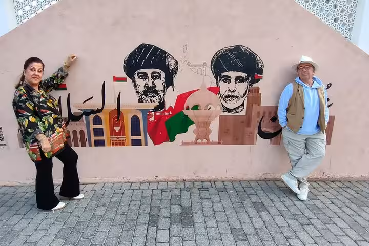 Tourists posing by colorful Omani mural near Muttrah Corniche during Muscat evening sightseeing with private taxi guide