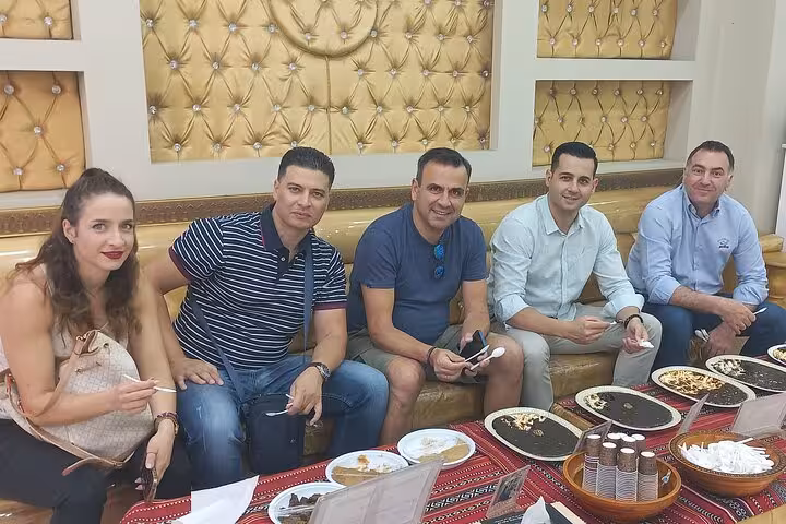 Group of travelers enjoy traditional Omani coffee and sweets on Muscat evening sightseeing taxi tour with cultural food tasting