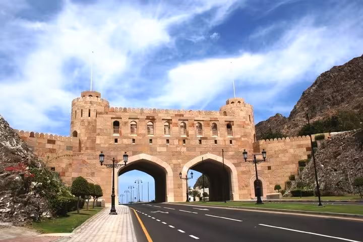 Historic Muscat city gate with twin towers and arched passages flanked by rocky mountains