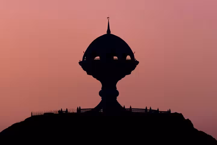 Silhouette of Muscat's iconic incense burner monument against a stunning pink evening sky during a heritage walking tour.