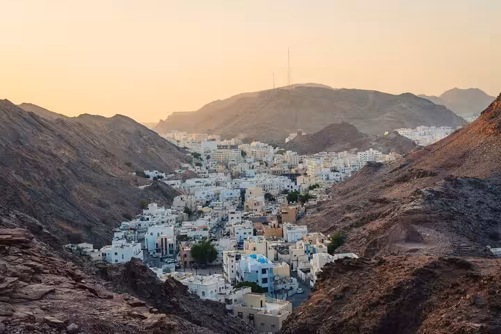 Panoramic sunset view of Muscat old quarter white buildings nestled between rocky mountains on evening walking tour