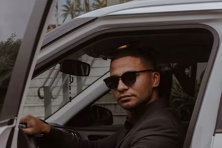Smartly dressed private driver in sunglasses sitting in a white car, ready for Muscat hotel and airport transfers