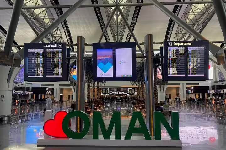 Departure area at Muscat Seeb International Airport featuring flight information screens and a welcoming Oman sign.