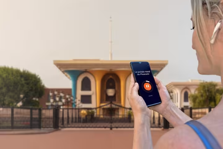 Tourist using audio guide app on smartphone in front of Al Alam Royal Palace in Muscat, Oman