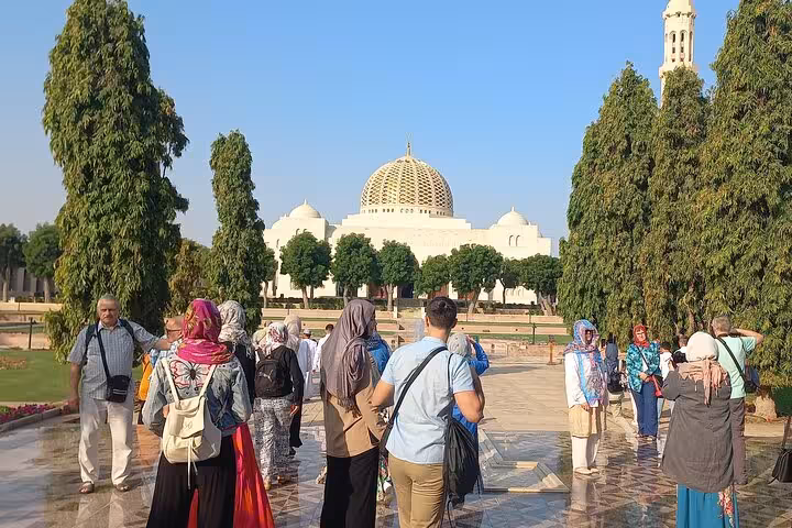 Tour group walking toward Sultan Qaboos Grand Mosque golden dome on a private Muscat sightseeing tour