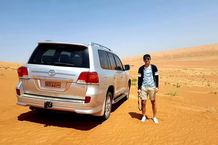 Traveler beside a 4x4 vehicle in the scenic desert en route from Muscat to Wadi Shab, ideal for adventure tours.