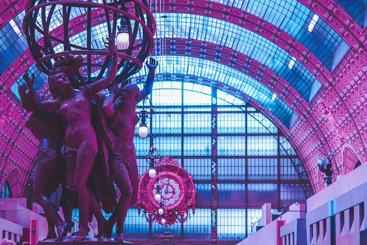 Bronze figures sculpture holding armillary sphere inside Musée d'Orsay's grand arched hall with ornate clock