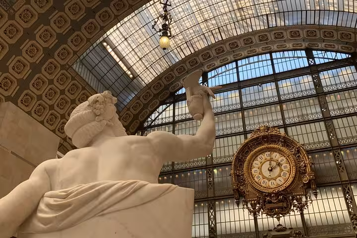 Marble statue and ornate gold clock inside the grand glass-roofed hall of Musée d'Orsay, Paris