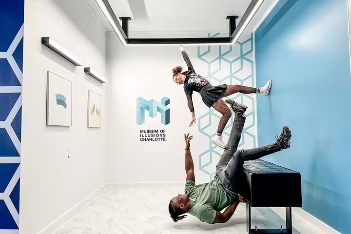 Two visitors posing at Museum of Illusions Charlotte, one lifted in air by person lying on floor
