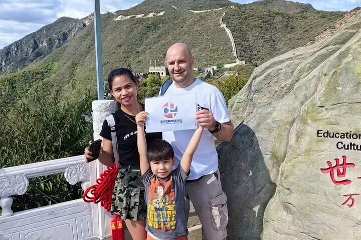 Happy family posing with a sign at Mutianyu Great Wall, showcasing a memorable private tour experience with an English-speaking driver.