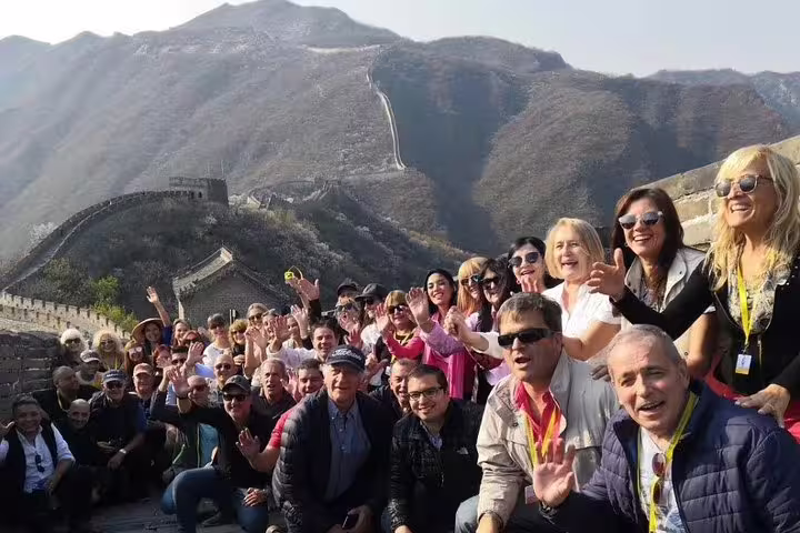 Large group of tourists smiling on Mutianyu Great Wall tour, highlighting camaraderie and stunning mountain views.