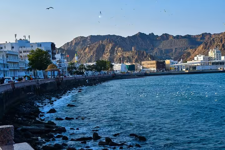 Daytime scene of Muttrah Corniche Muscat with turquoise sea, rocky shoreline and mountain backdrop on classic sightseeing taxi tour