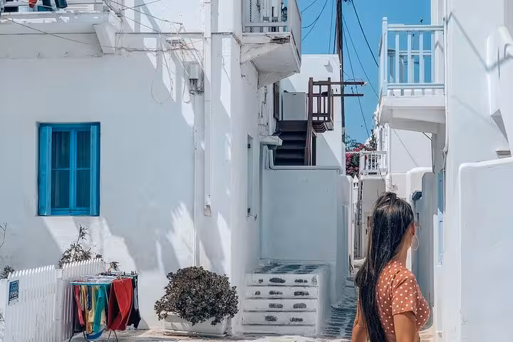 Cruise travelers walking Mykonos Chora alley with whitewashed houses, blue windows and seaside steps