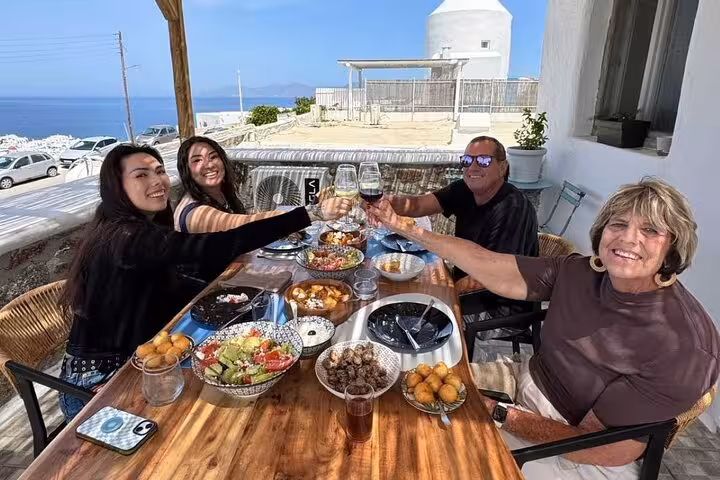 Guests toast with wine over homemade Greek dishes at a Mykonos cooking class with Aegean sunset views