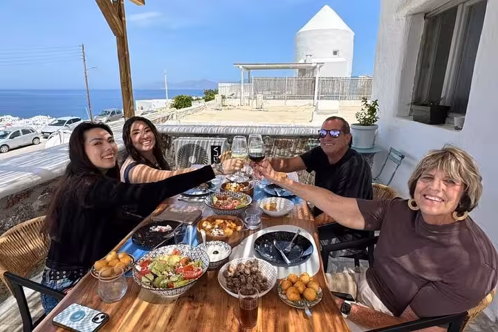 Small group Mykonian cooking class guests toast with wine over a Greek mezze lunch on a Mykonos terrace