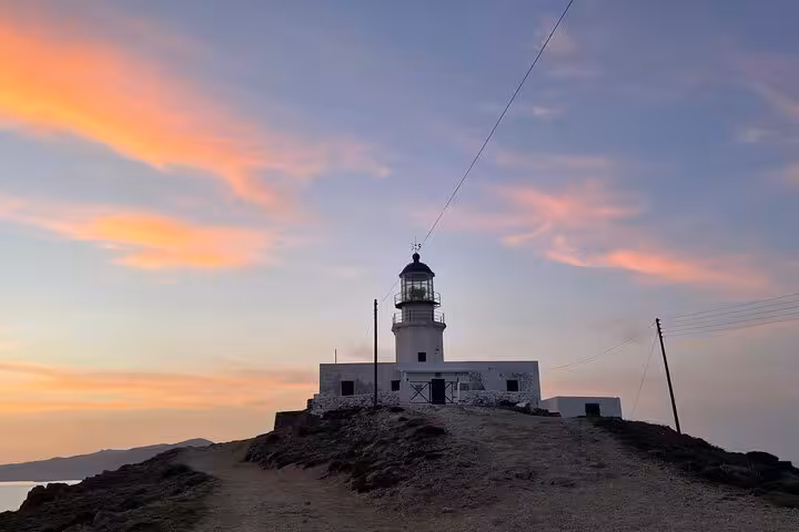 Sunset view of Mykonos lighthouse on rocky coast, a highlight of a private half-day island tour