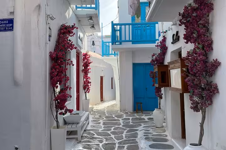 Charming Mykonos Old Town alley with bougainvillea, blue doors and stone path on island sights tour