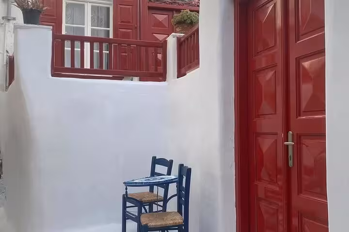 Charming Mykonos old town alley with red door and blue chairs, featured on a private Mykonos experience