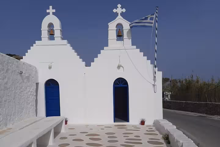 Traditional white Mykonos chapel with blue doors and Greek flag, cultural stop on a half-day private island tour