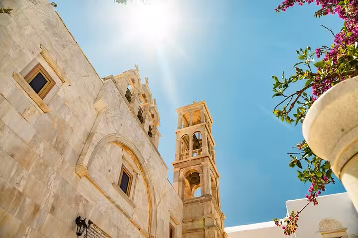 White stone church and bell tower under blue sky in Mykonos, cultural landmark on a private guided tour