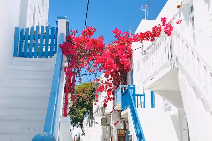 Whitewashed Mykonos alley with blue balconies and pink bougainvillea, charming scene on a private island tour