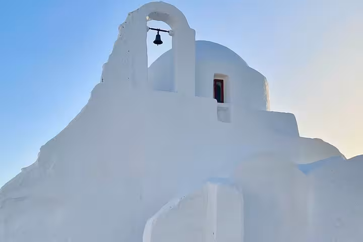 Whitewashed Mykonos church with bell and dome in golden light, a highlight on island sights tour