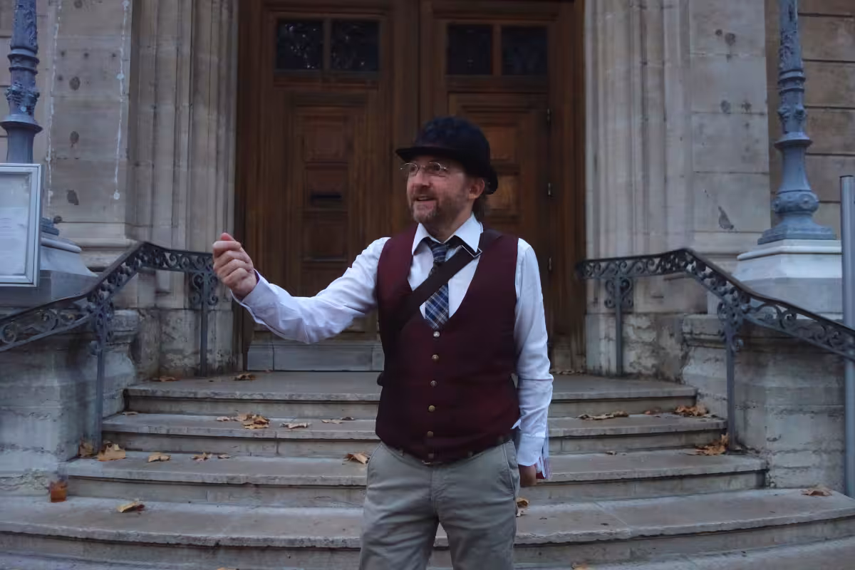 Tour guide in vintage vest and bowler hat gesturing in front of historic Lyon stone building