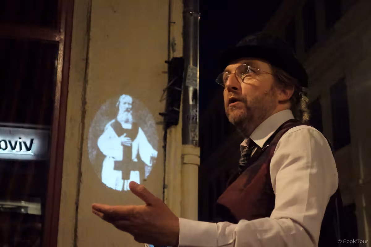 Tour guide gesturing at night with historical figure projected on Lyon building wall