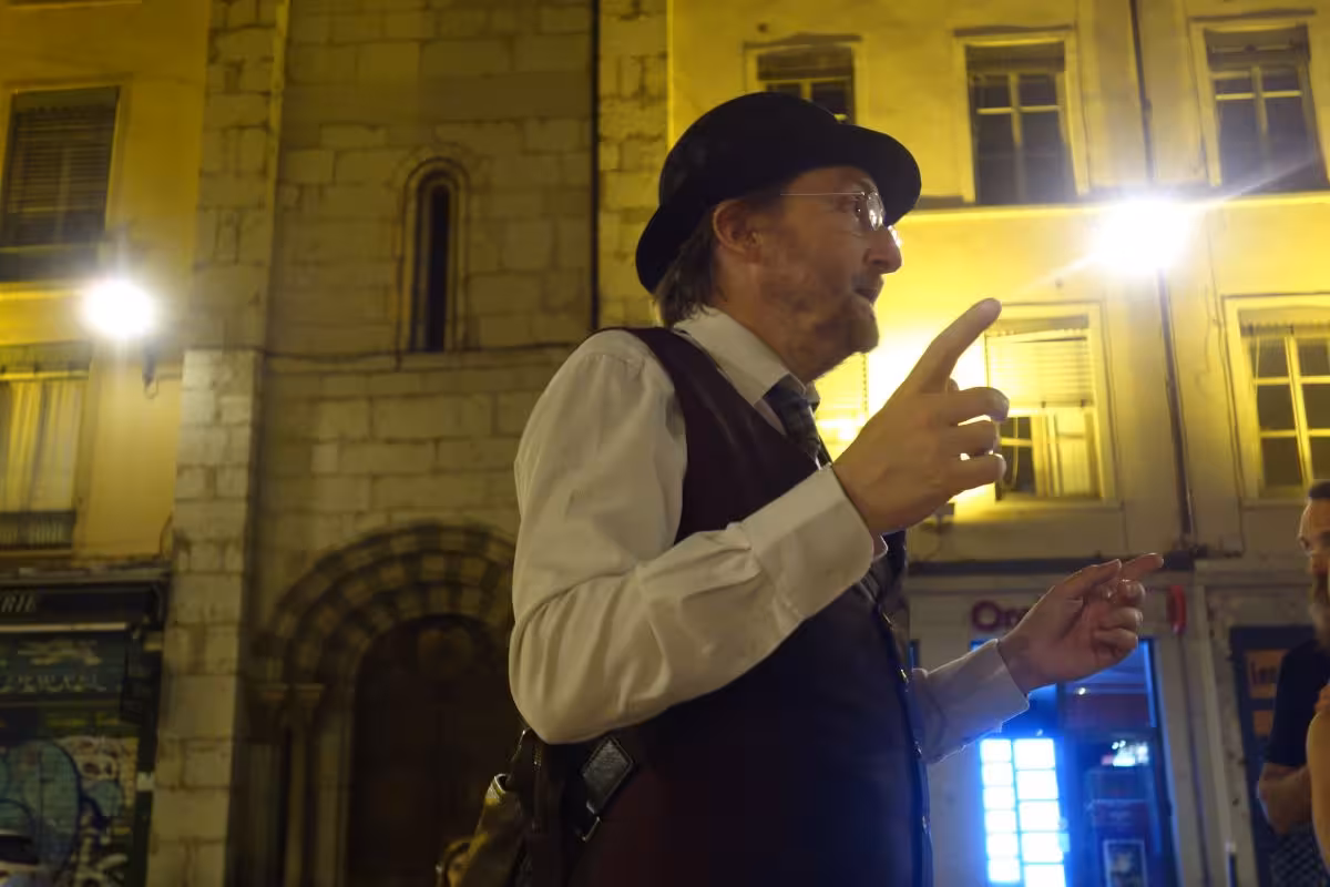 Costumed guide in bowler hat gesturing dramatically during a night walking tour in Lyon