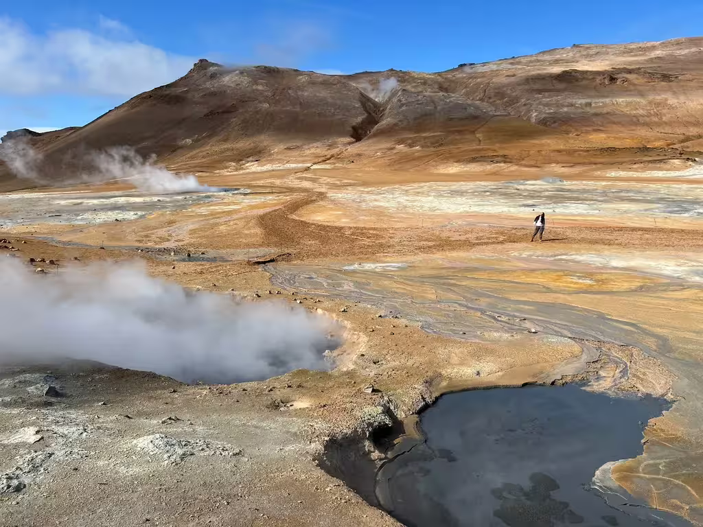 Steaming geothermal hot springs and mud pools at Myvatn with colorful mineral deposits and volcanic hills