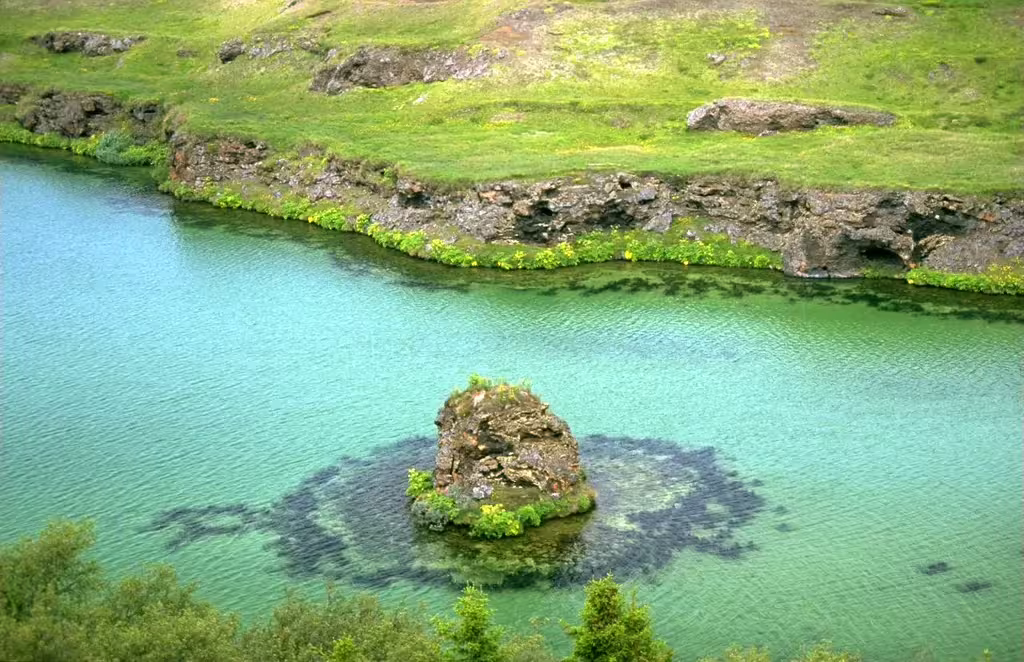 Turquoise waters of Myvatn Lake with volcanic rock formation and green lava shores in Iceland
