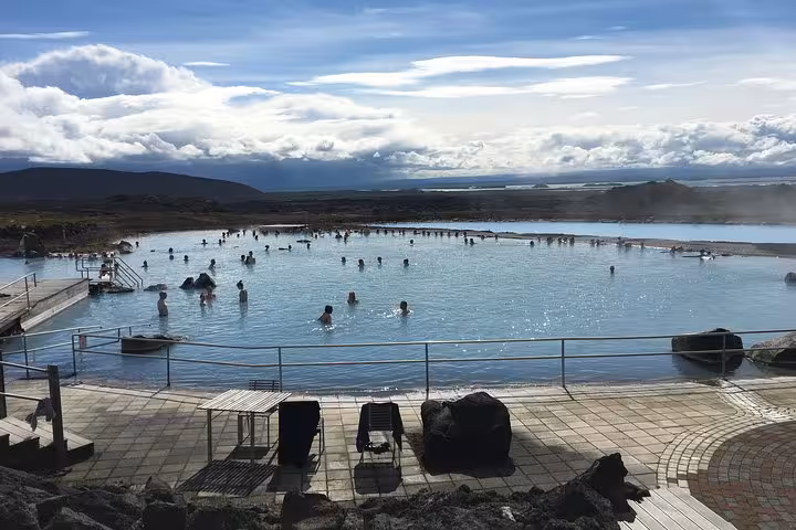 Visitors enjoy the natural geothermal waters of the Myvatn Nature Baths under a bright sky, part of the Akureyri day tour.