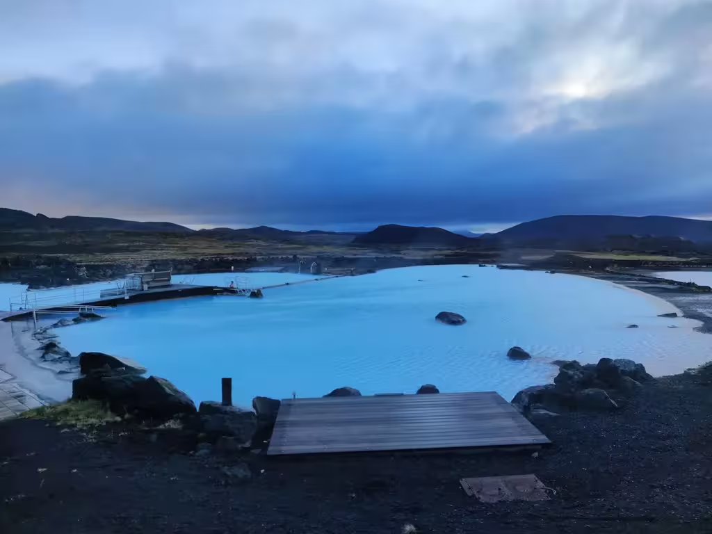 Milky blue geothermal waters of Myvatn Nature Baths at dusk with volcanic landscape and dramatic cloudy sky