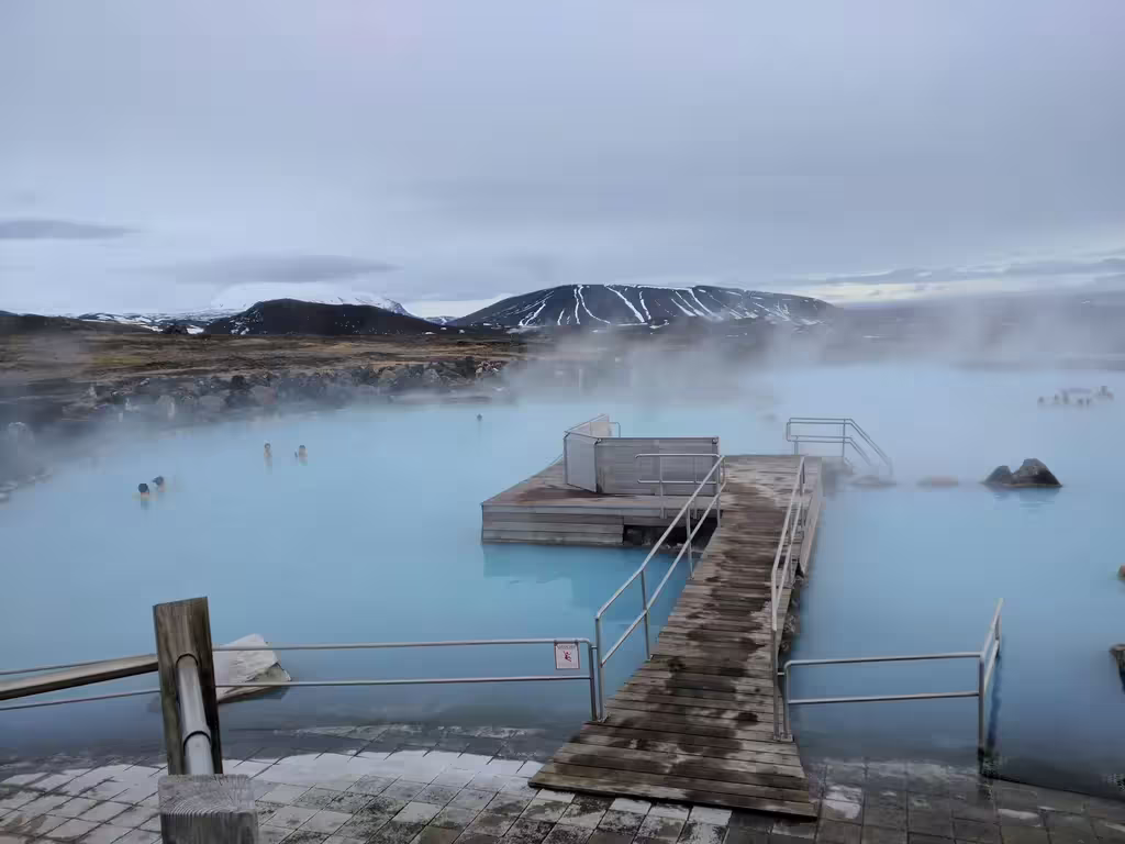 Steaming milky-blue geothermal waters of Myvatn Nature Baths with snow-capped volcanic mountains in Iceland