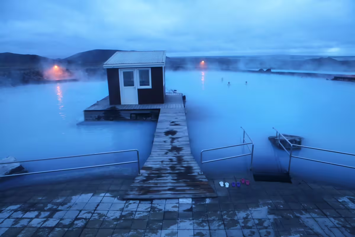 Steaming blue geothermal waters of Myvatn Nature Baths at dusk with wooden dock and small cabin